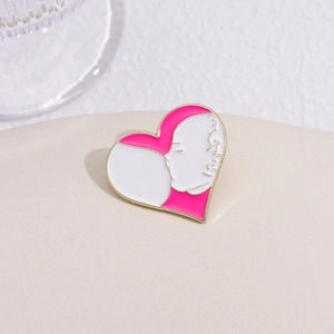 Artistic heart-shaped enamel brooch with magenta and white facial profile on beige surface
