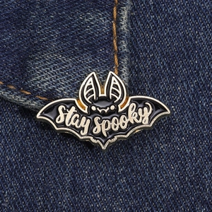 Détail d'un pin's chauve-souris en émail noir avec texte Stay Spooky sur tissu denim