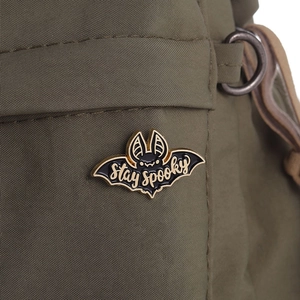Gros plan d'un pin's chauve-souris en émail noir avec texte Stay spooky sur toile