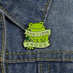 Cartoon green frog enamel pin with I Love Frogs banner on blue denim jacket