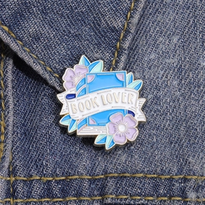 Book Lover enamel pin with blue book and flowers pinned on a denim jacket pocket