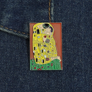 Detail of Gustav Klimt The Kiss enamel brooch pinned on dark blue denim fabric texture