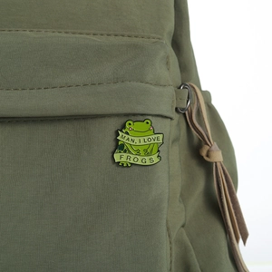Macro shot of an enamel green frog pin with I Love Frogs text on a green canvas bag