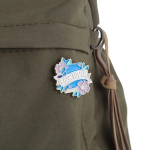 Artistic enamel Book Lover brooch with purple flowers on a green canvas backpack