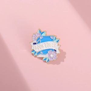 Blue enamel book lover brooch with purple flowers and gold details on pink background