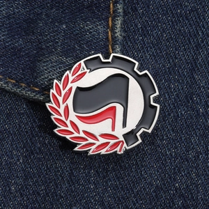 Close-up of red and black flag pin with industrial gear and laurel on denim fabric