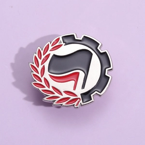 Detail of metal enamel pin featuring red and black flags with gear and laurel wreath