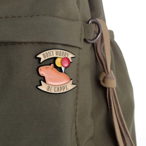 Close-up of a cute capybara enamel pin with balloons on a green canvas bag
