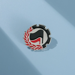 Macro shot of a metal enamel pin featuring red and black flags with laurel leaf and gear details