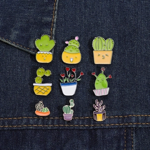 Set aus neun bunten Emaille-Broschen mit Kakteen und Sukkulenten auf dunklem Denim-Stoff