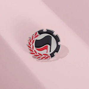 Antifa-style round metal enamel pin with red laurel and black gear on pink background