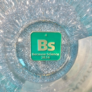 Close-up of a green enamel 'Because Science' pin badge in a glittery lab container