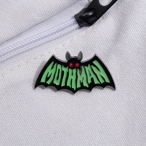 Macro detail of Mothman enamel pin with red eyes on white canvas bag with zipper
