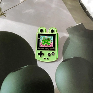 Detail of green enamel frog game console pin with pixel art and engraved buttons