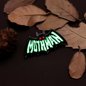 Luminous Mothman enamel pin with glowing green text on black metal bat silhouette