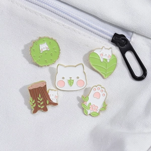 Detail of five cute cat and plant enamel pins attached to a white canvas zipper bag