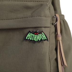 Detailed close-up of a Mothman enamel pin attached to a green canvas bag