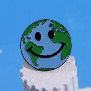 Broche émaillée en forme de Terre avec visage souriant sur socle blanc, fond bleu clair