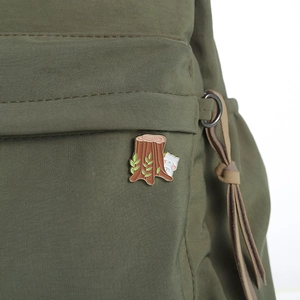 Macro shot of an enamel pin with a cute white cat peeking from a brown tree stump with leaves