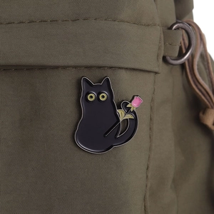 Détail d'un pin's chat noir mignon avec rose rose sur un sac à dos en toile verte