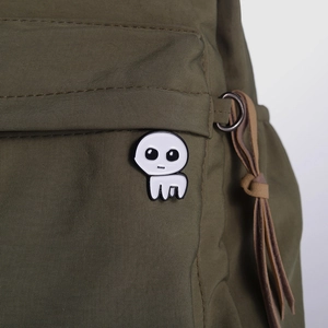 Close-up of white TBH creature enamel pin attached to an olive green fabric bag