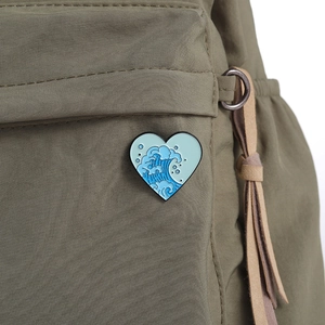 Detail of a heart-shaped enamel pin with ocean wave pattern on a canvas backpack