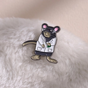 Detail view of a cartoon mouse enamel pin wearing a white lab coat with a green vial