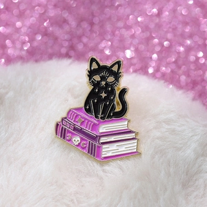 Makro-Detail der Emaille-Anstecknadel: Schwarze Katze auf lila Zauberbüchern mit Goldrand