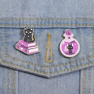 Set aus zwei magischen schwarzen Katzen-Emaille-Pins mit lila Hüten und Tränken auf Denim