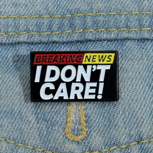 Dettaglio della spilla smaltata Breaking News I Don't Care su denim con bordo in metallo