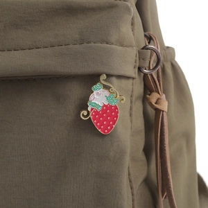 Detail view of a cute rabbit strawberry enamel pin attached to a green nylon backpack