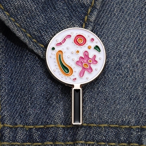 Spilla smaltata con batteri colorati sotto una lente d'ingrandimento su denim