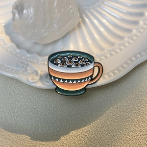 Detailed view of surrealist enamel coffee cup badge with eyeball design on white shell tray