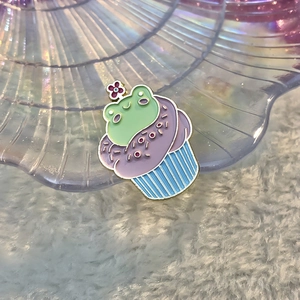 Detalle del pin esmaltado de cupcake rana en bandeja decorativa con fondo de felpa suave