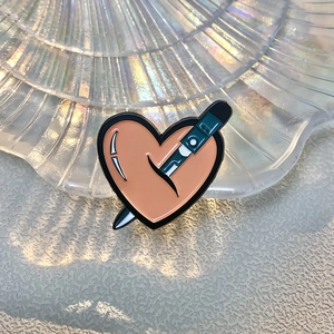 Macro shot of an enamel heart pin with a pen detail in a shell-shaped glass dish