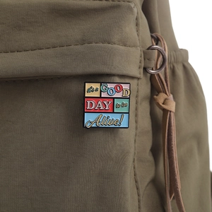 Detail of square colorful enamel pin with positive slogan on green canvas bag