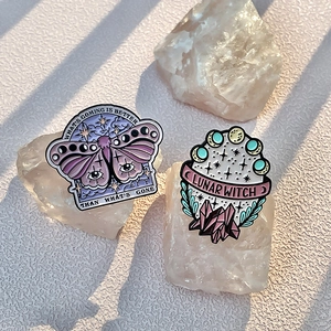 Skull magic and purple butterfly enamel pin set displayed on white mineral stone