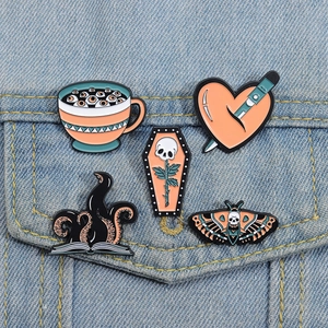 Close-up of five gothic enamel pins including skulls and hearts on denim jacket