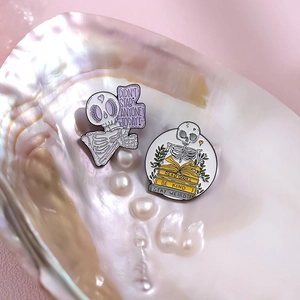 Detail of skull enamel pins with witty slogans placed inside an iridescent pearl shell