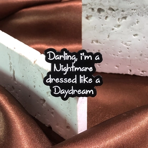 Detail of black cloud enamel brooch with white text Darling, I'm a Nightmare on stone