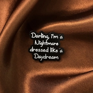 Detailed view of black enamel pin with text on soft brown satin silk background