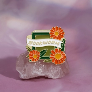 Golden enamel bookworm badge pin with floral details on a decorative stone
