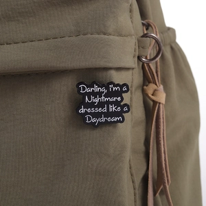 Vue macro d'une broche en émail noir avec citation sur un sac en nylon vert