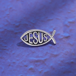 Detailed view of a vintage silver Jesus fish brooch with cutout letters on blue surface