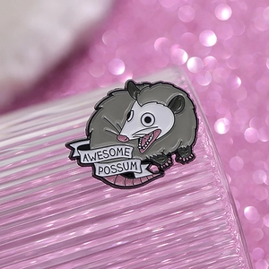 Detail of Awesome Possum enamel pin with cartoon animal design on pink background