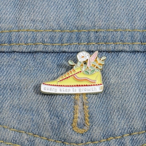 Yellow sneaker enamel pin with flowers and 'every step is growth' quote on denim
