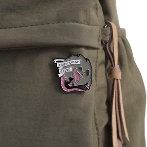 Funny possum enamel pin with I EXIST OUT OF SPITE text on an olive canvas bag