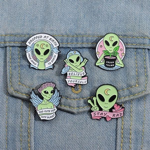 Dettaglio di spille smaltate aliene verdi su una giacca di jeans con slogan creativi