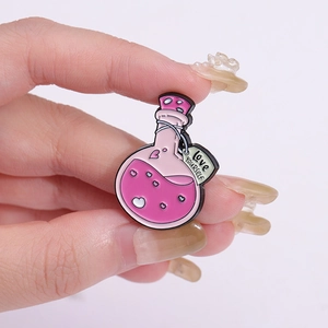 Detail showing enamel heart potion bottle brooch with Love Yourself tag held in fingers
