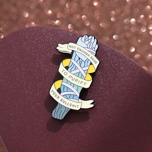 Macro shot of sage bundle enamel pin with funny quote on dark leather background